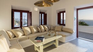 A modern living room with a beige sofa, a wooden coffee table, and a view of the sea through large windows.