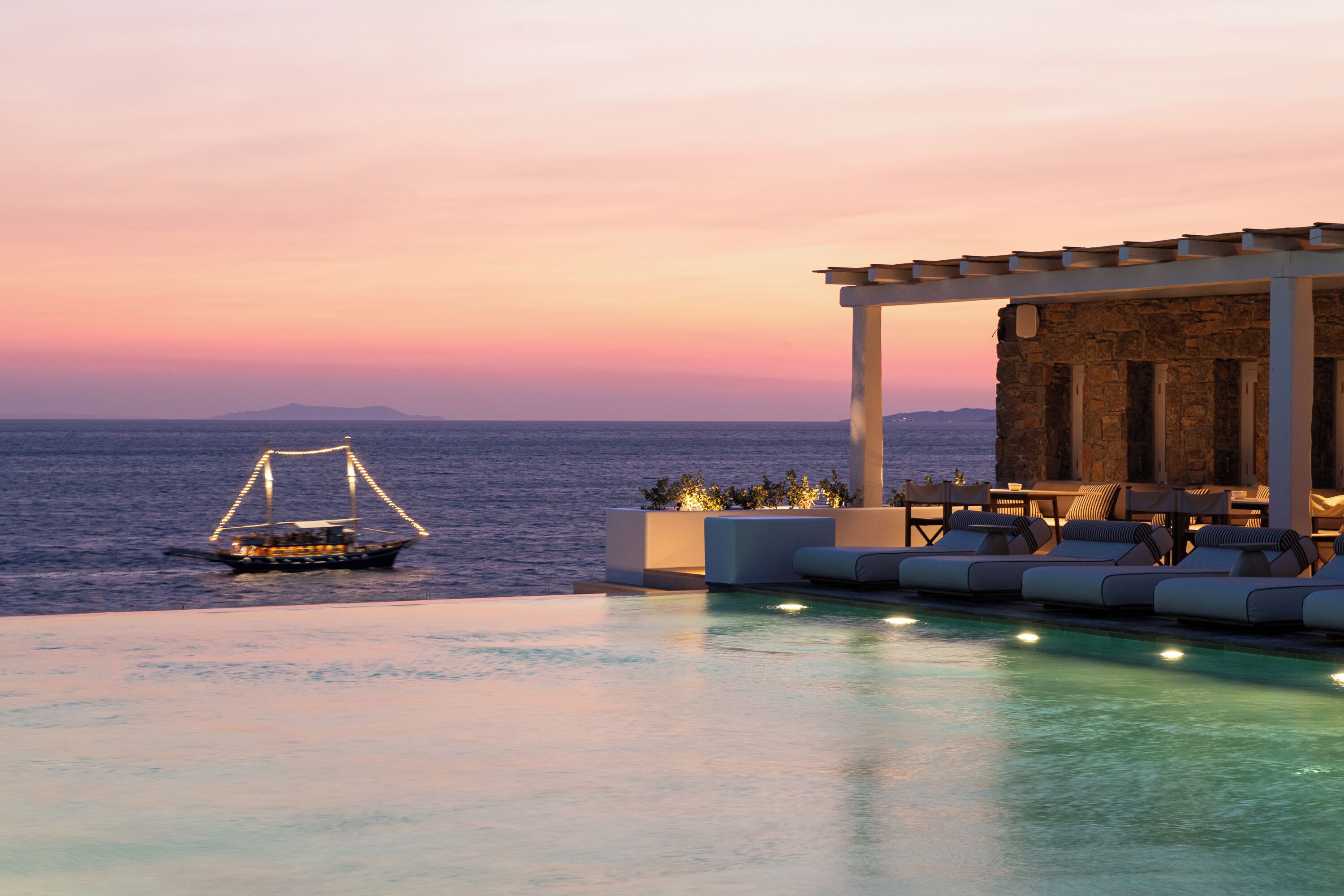 An infinity pool with a view of the sea and a boat at sunset.