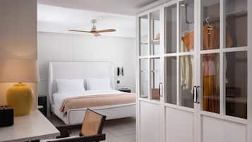 A bedroom with a bed, a chair, a desk with a lamp, a wardrobe with glass doors, and a ceiling fan.