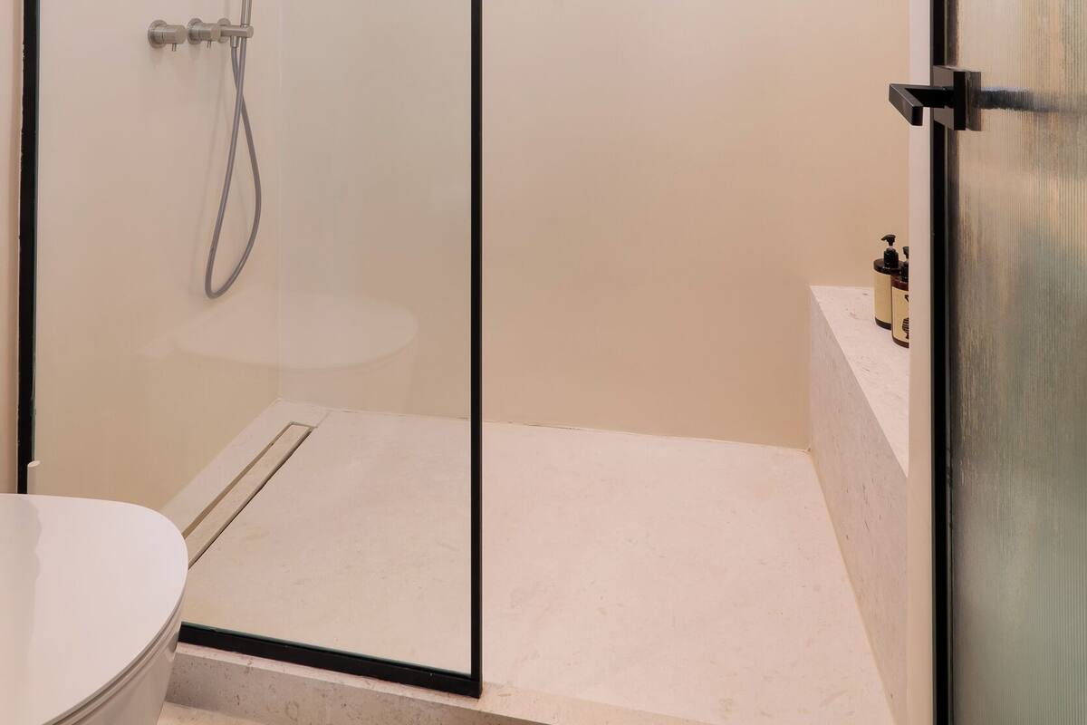 A modern bathroom with a glass-enclosed shower, a toilet, and a small window.
