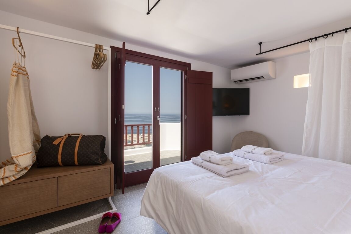Ein Hotelzimmer mit Bett, einer Sitzecke, einem Koffer, Schuhen, einem Fernseher und einem Balkon mit Blick.