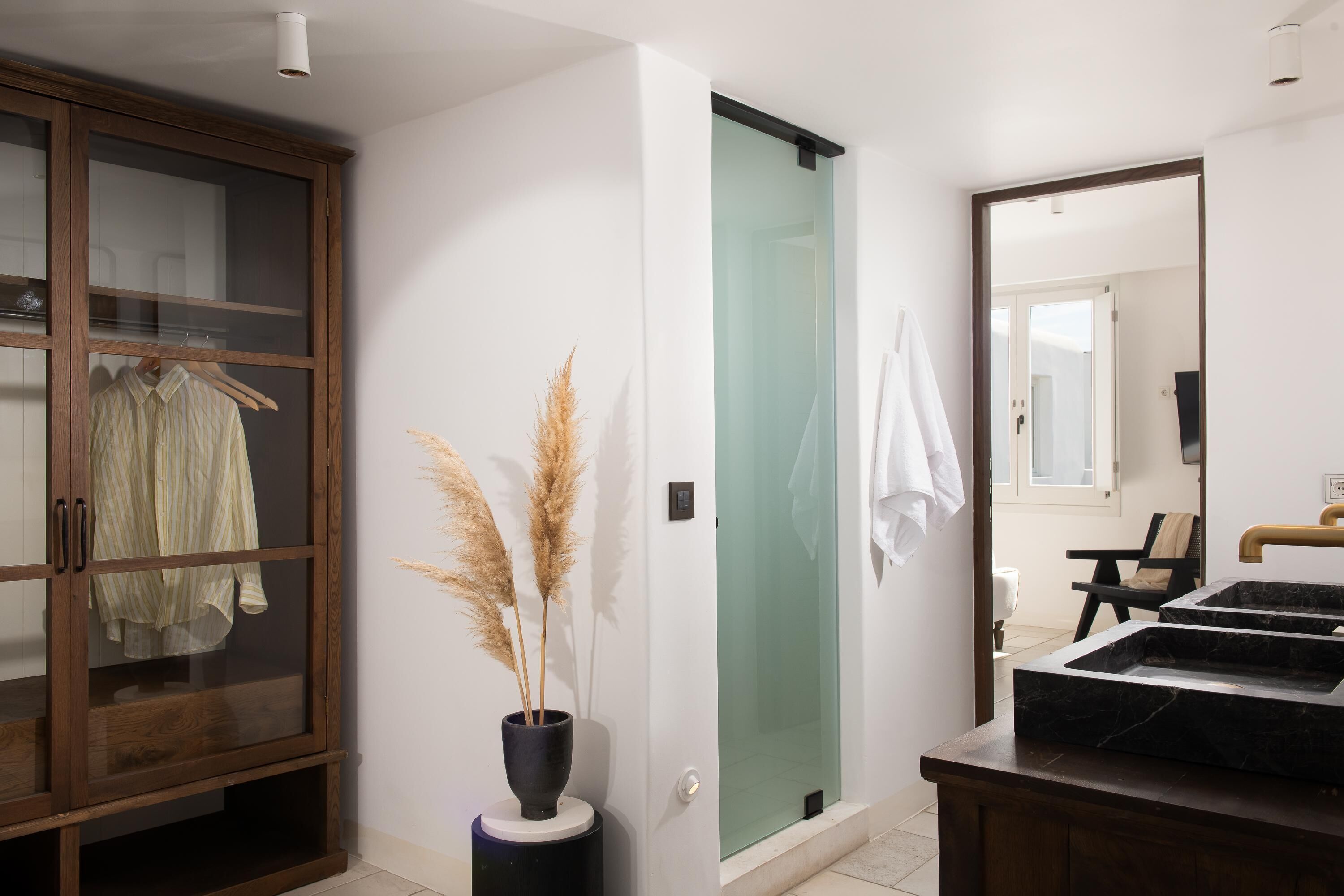 Un baño moderno con ducha de vidrio, un mueble de madera con una prenda colgada y un lavabo de mármol negro.