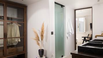 Un baño moderno con ducha de vidrio, un mueble de madera con una prenda colgada y un lavabo de mármol negro.