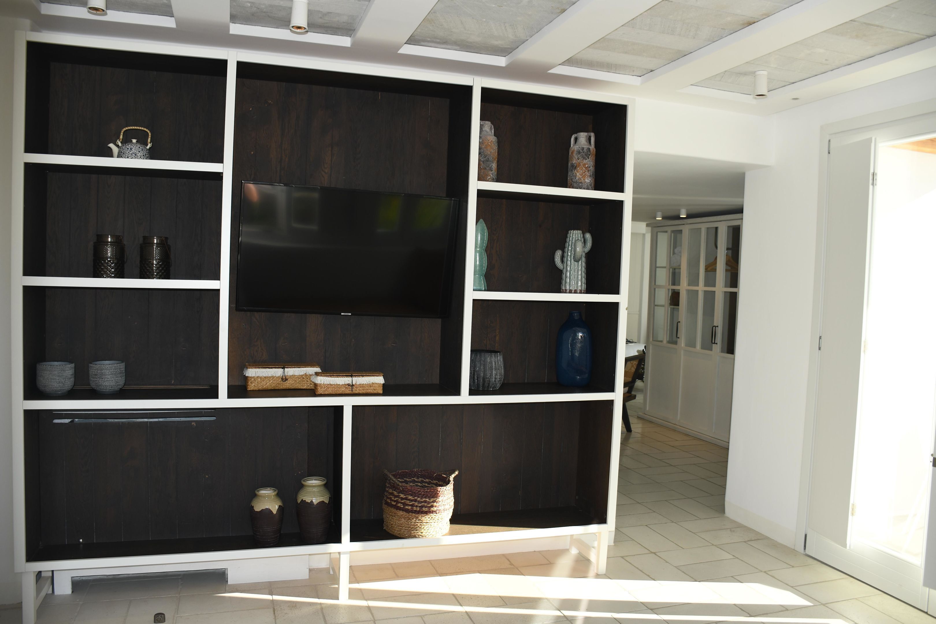 A modern living room with a large dark wood shelving unit, a flat-screen TV, and various decorative items.