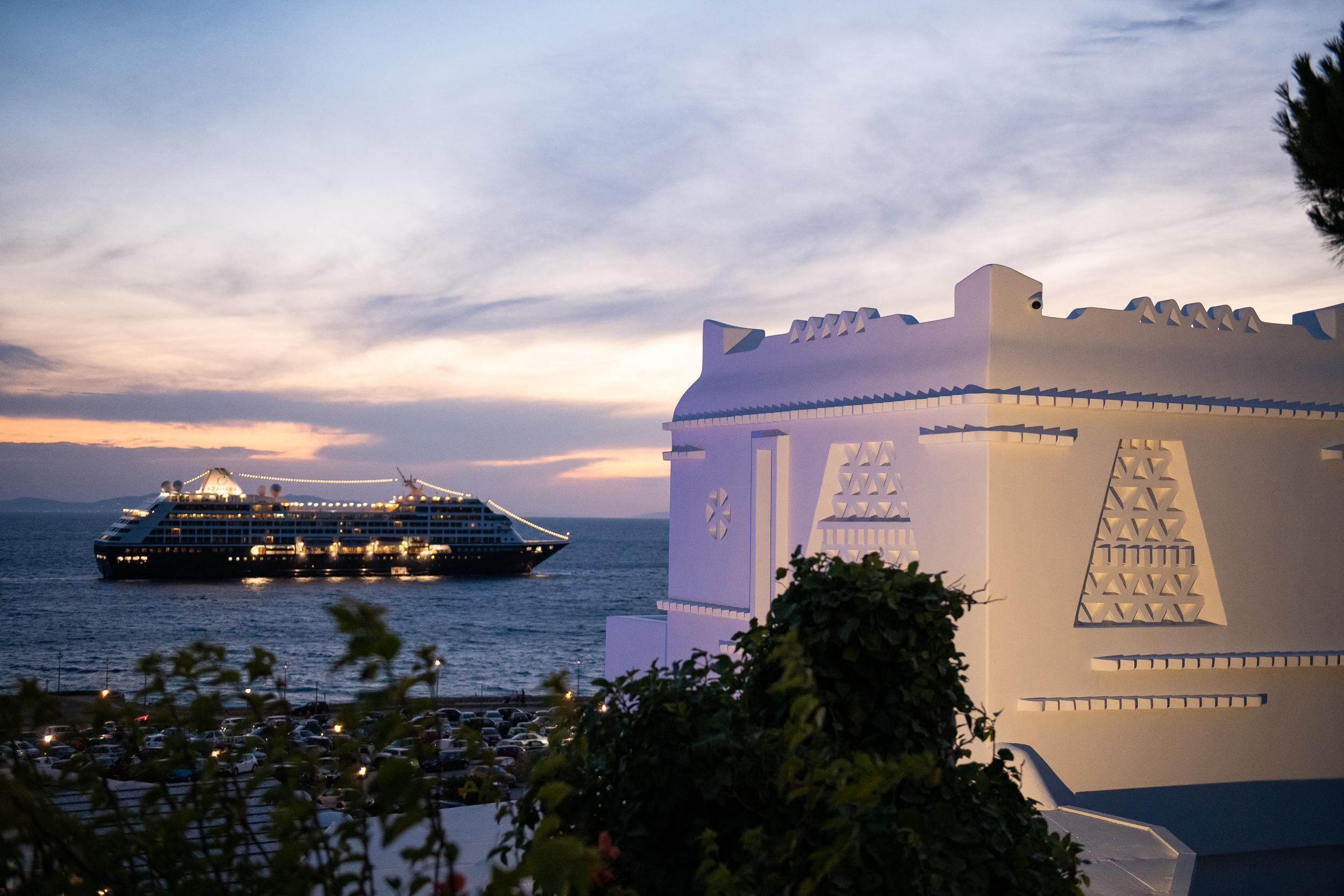 A cruise ship docked at a port with a large white building featuring geometric patterns in the foreground.