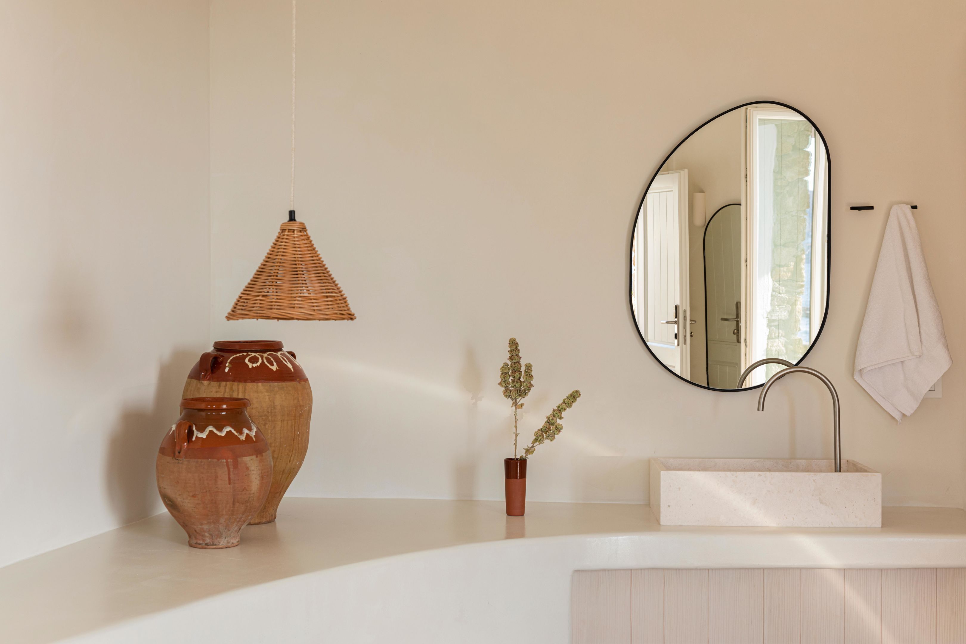 Une salle de bain avec un lavabo blanc, un miroir rond, une suspension et deux vases.