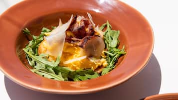 A bowl of food with greens, eggs, and bacon.
