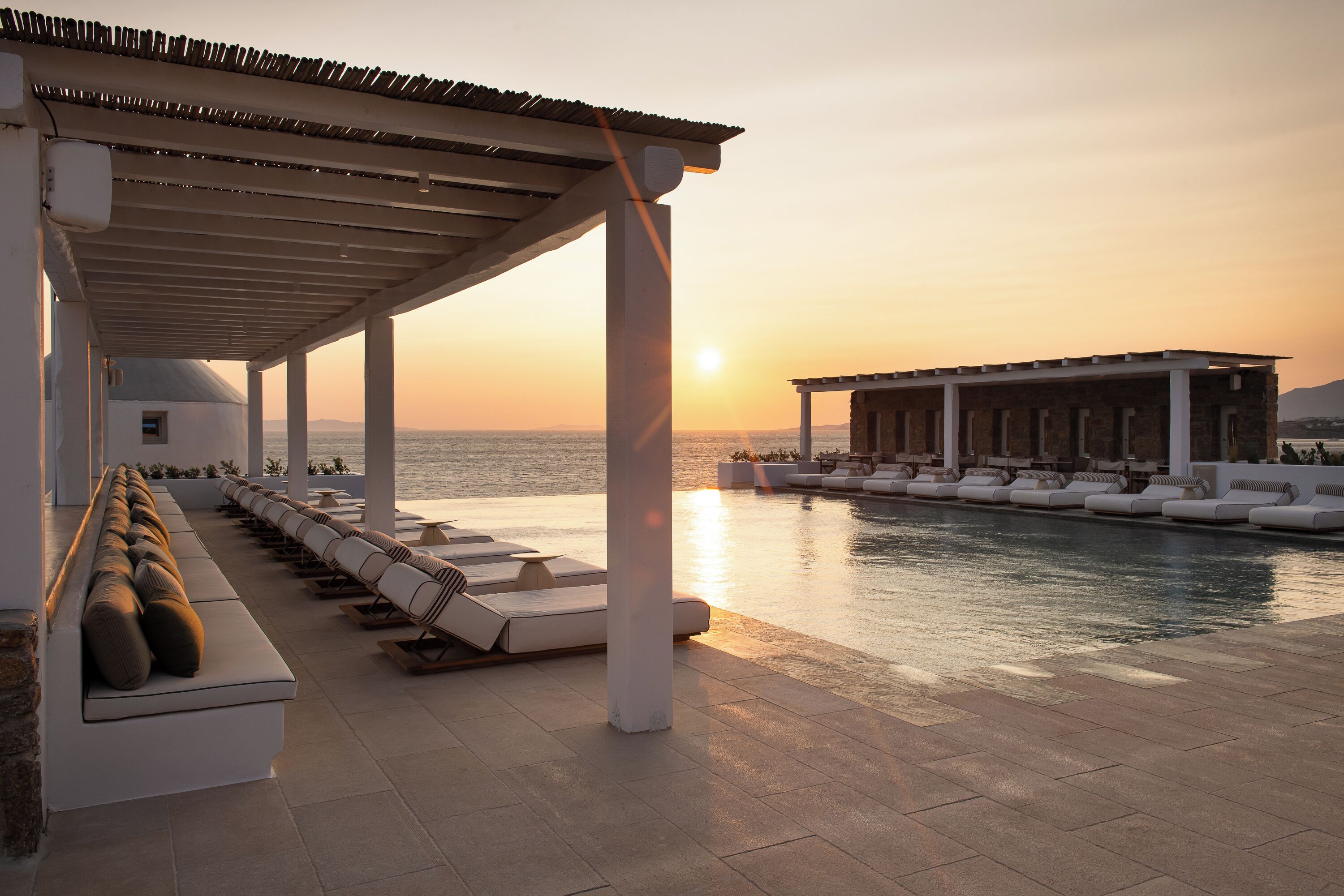 A poolside area with lounge chairs and a covered seating area, overlooking the sea.