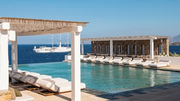 Zona de piscina con sillas de descanso y un área de estar cubierta, con vista al mar.