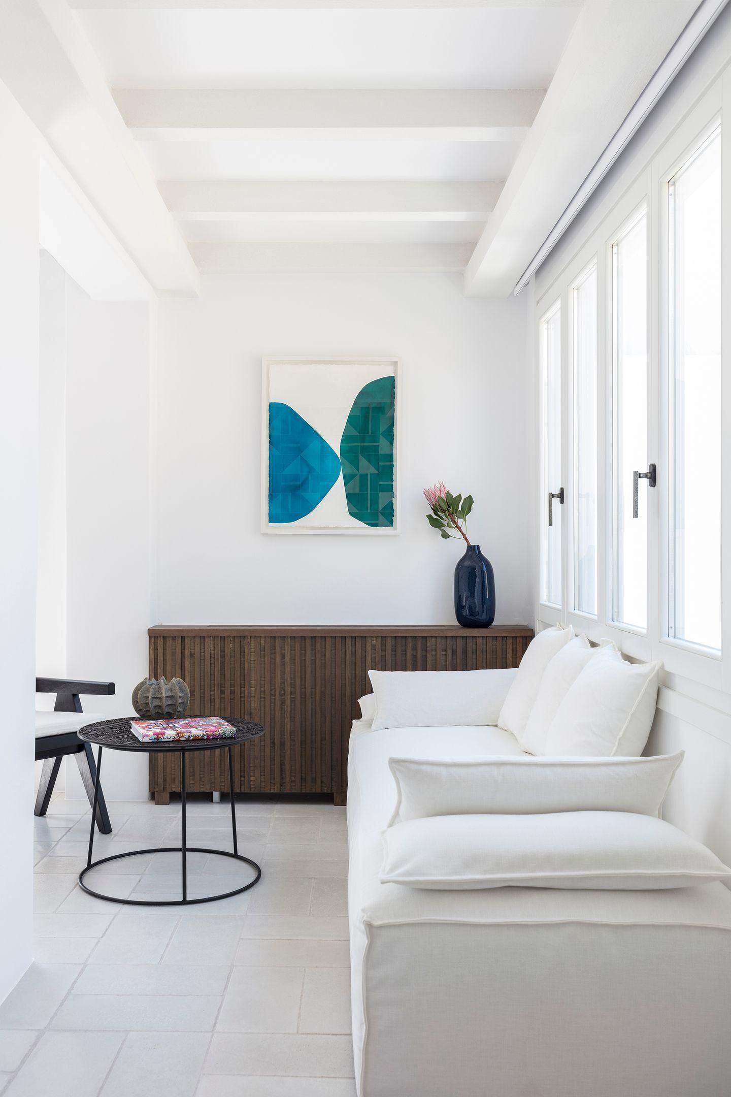 A modern living room with a white sofa, a round table, and a blue vase with flowers.