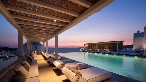 A poolside lounge with sun loungers and a view of the sea at dusk.