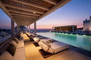Un salon au bord de la piscine, avec des chaises longues et une vue sur la mer au crépuscule.