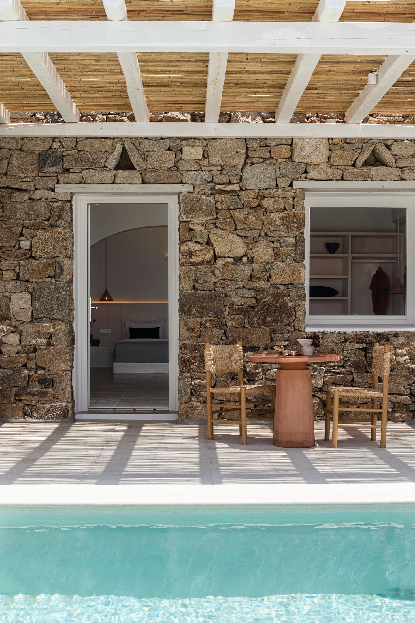 A stone-walled room with a bed, a window, and a table with chairs.
