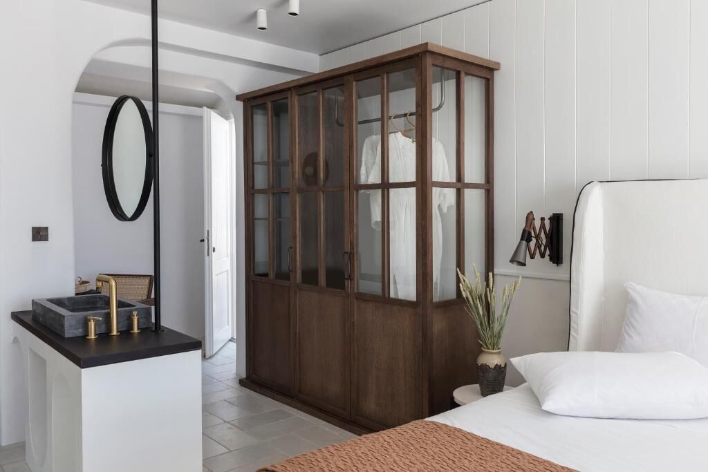 A bedroom with a bed, a wooden wardrobe, a small sink, and a mirror.