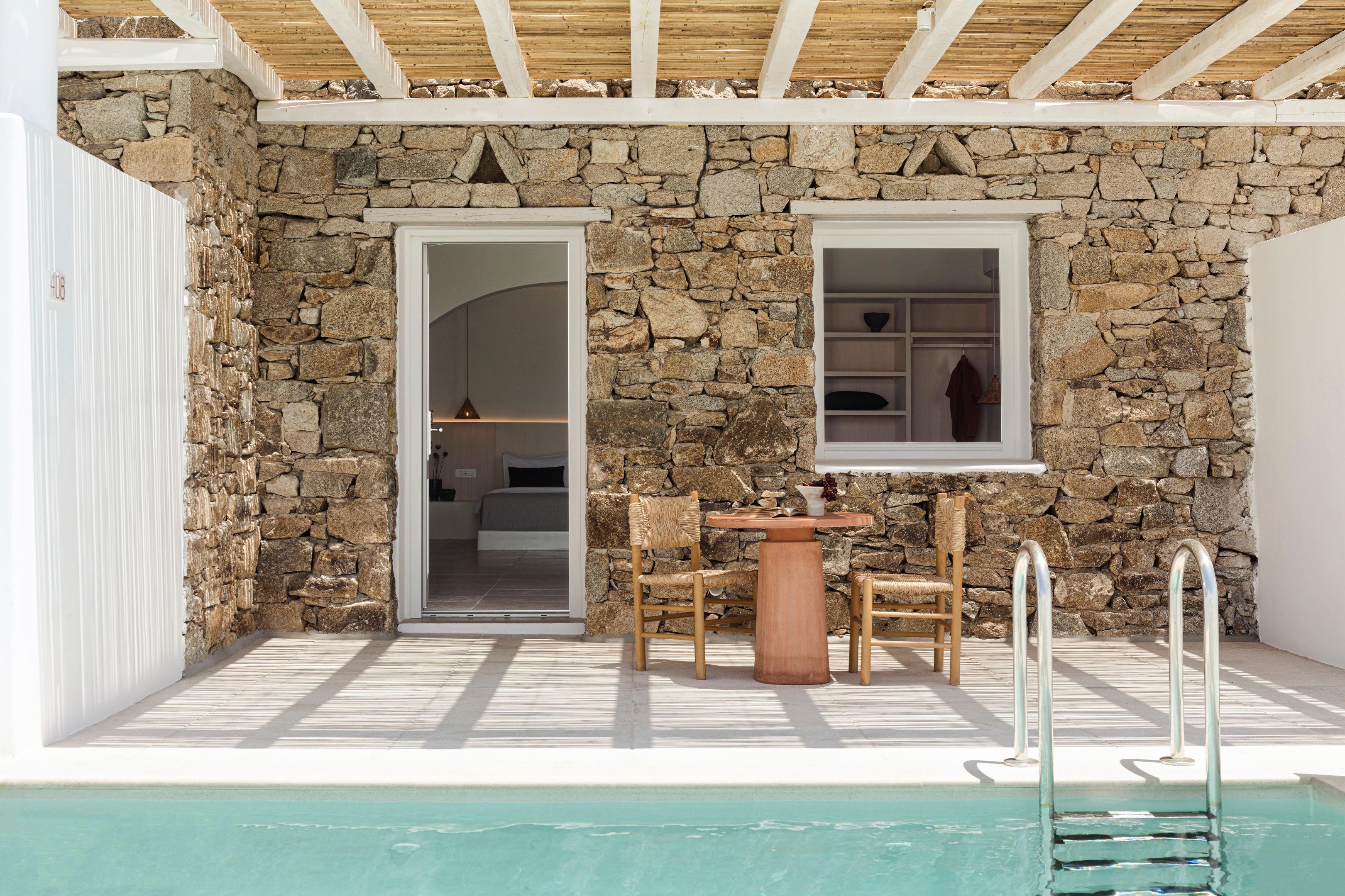 A stone-walled room with a wooden ceiling, a pool, and a table with chairs.