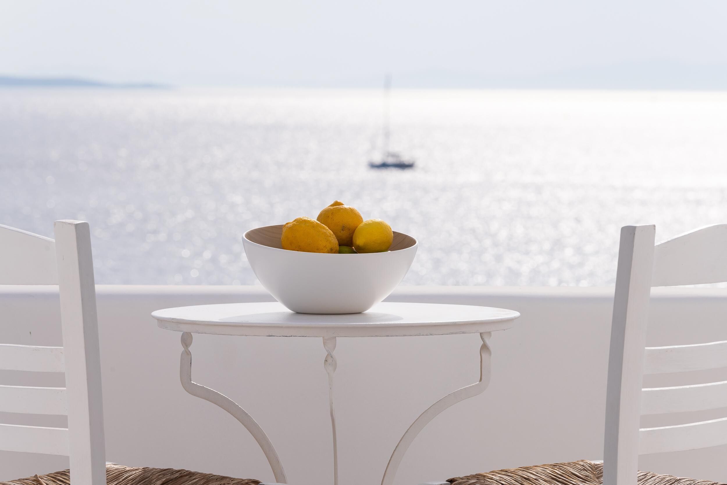 A white table with a bowl of lemons on a balcony overlooking the sea.