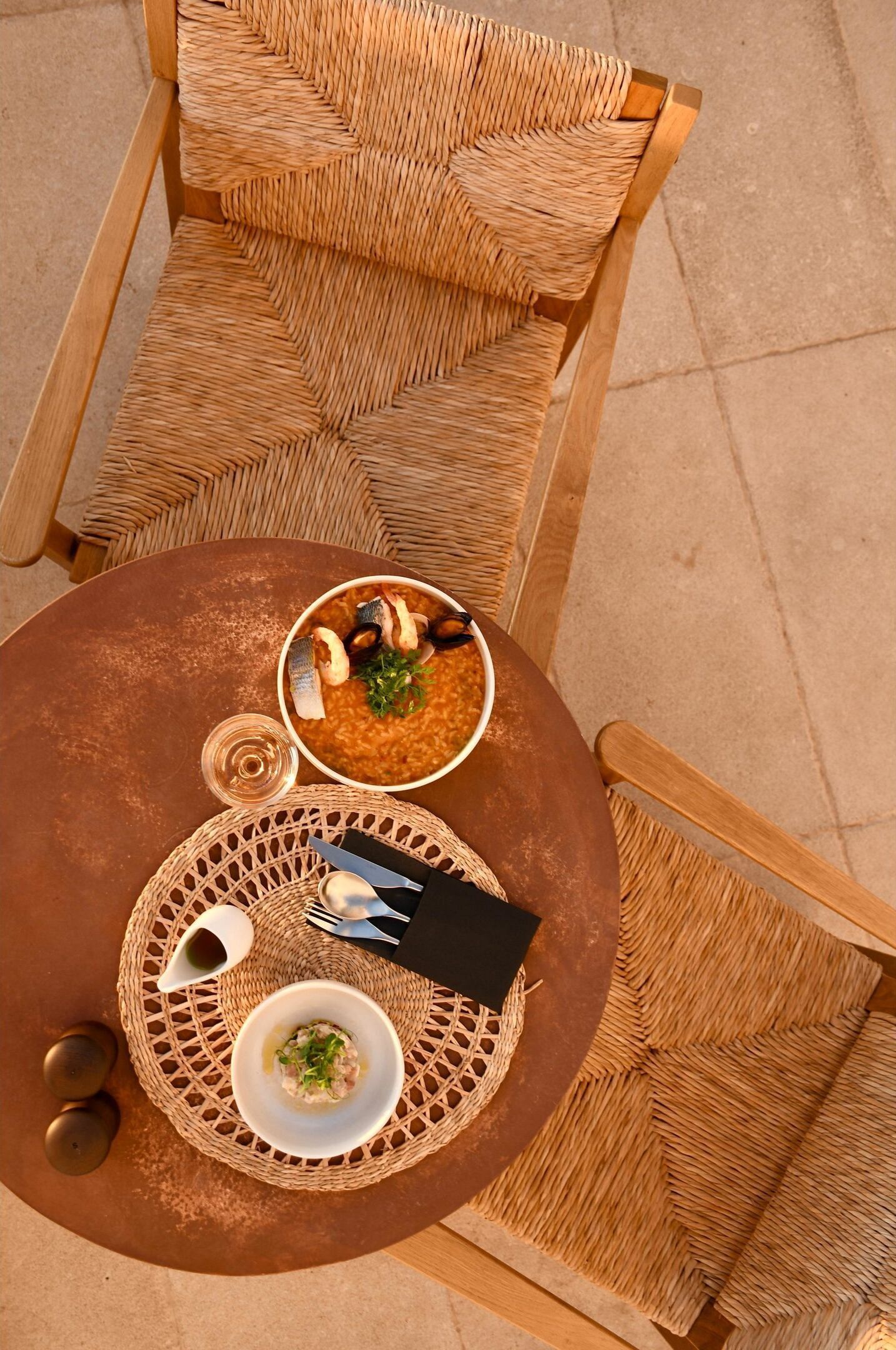 A round table with two bowls of food, a napkin, cutlery, and a glass.