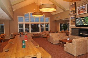 A spacious living area with a large wooden table, comfortable seating, a fireplace, and large windows. - Lakeview Signature Inn Calgary Airport (Calgary)