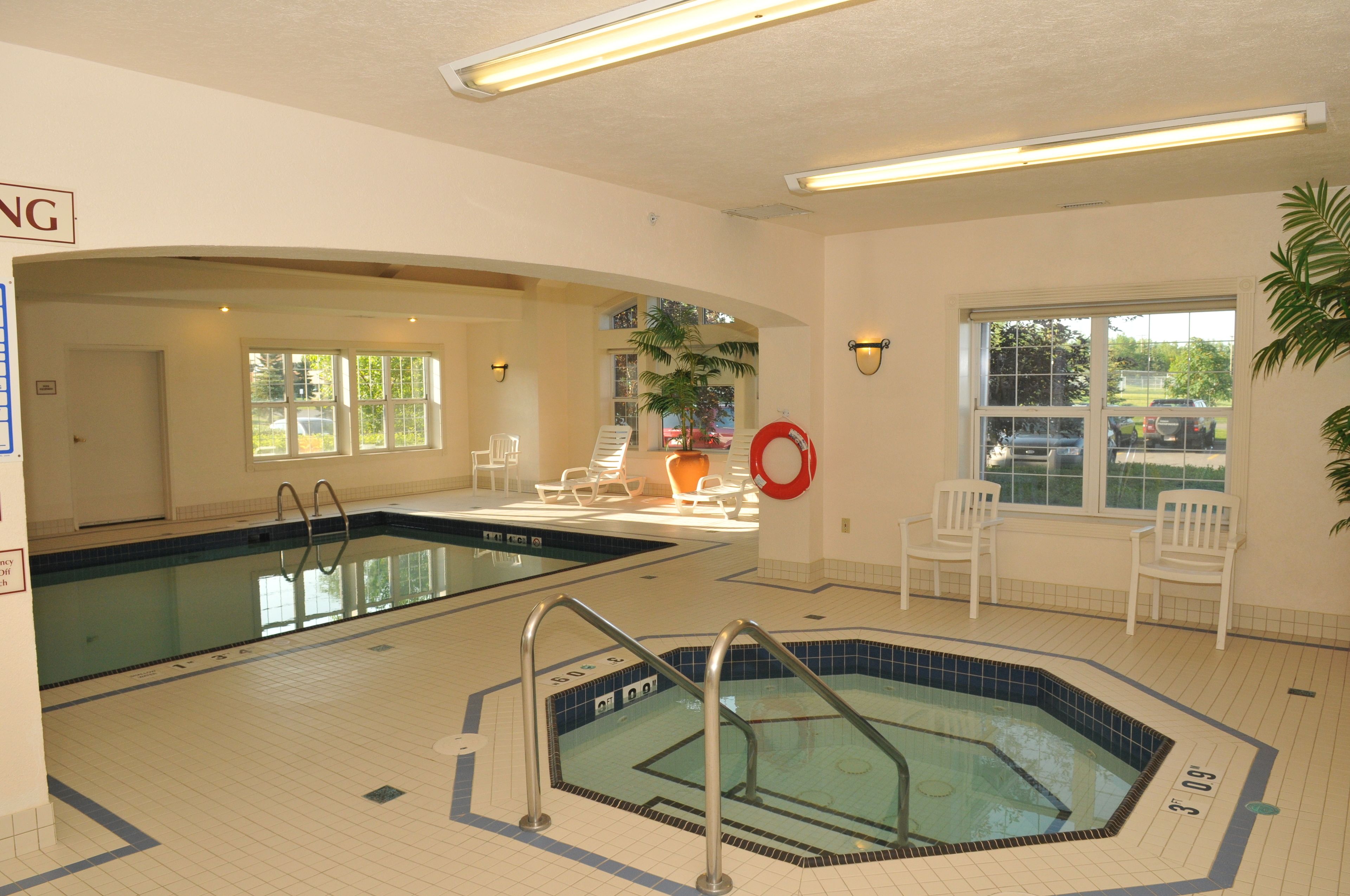 An indoor swimming pool with two lanes, lounge chairs, and a hot tub.