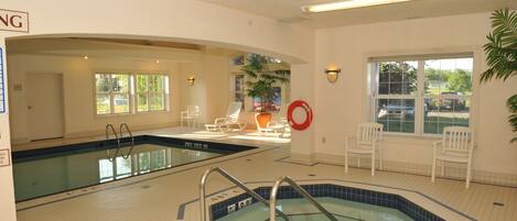 An indoor swimming pool with two lanes, lounge chairs, and a hot tub.