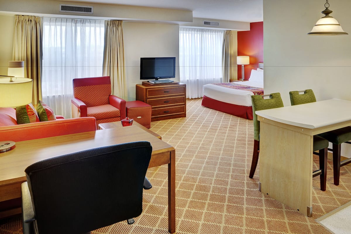 A hotel room with a bed, a desk with a chair, a television on a dresser, and a dining table with chairs.