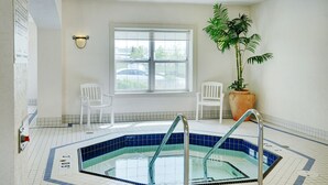 Un área de piscina con suelo de baldosas, una piscina con barandillas de metal, dos sillas blancas, una planta grande en maceta y una ventana con vistas al exterior.