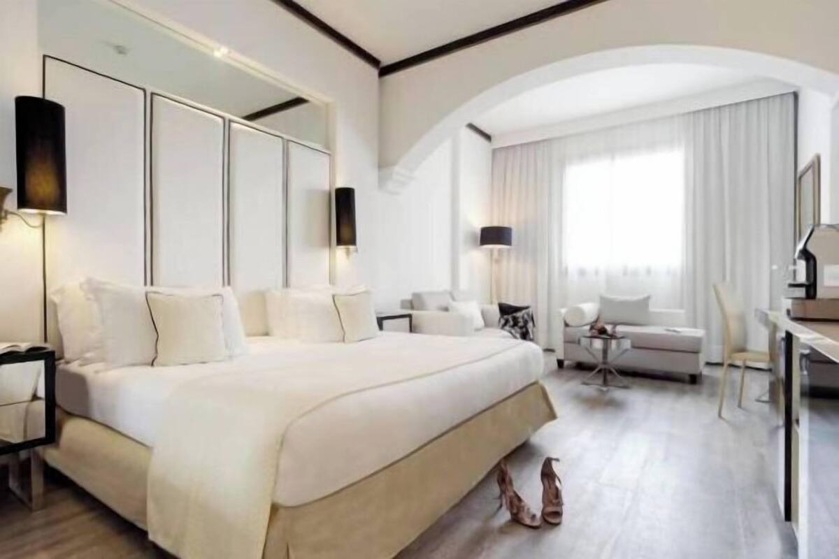 A hotel room with a large bed, a desk, a chair, and a sofa.