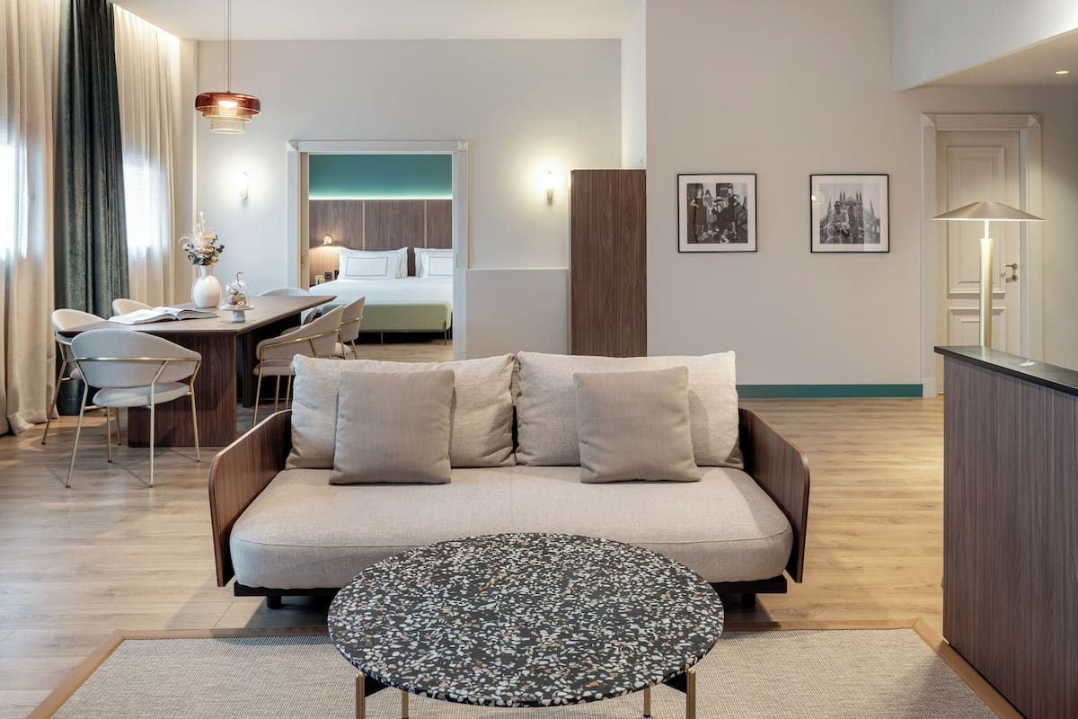 Une chambre d’hôtel moderne dotée d’un canapé, d’une table basse ronde, d’un coin repas et offrant une vue sur la ville.