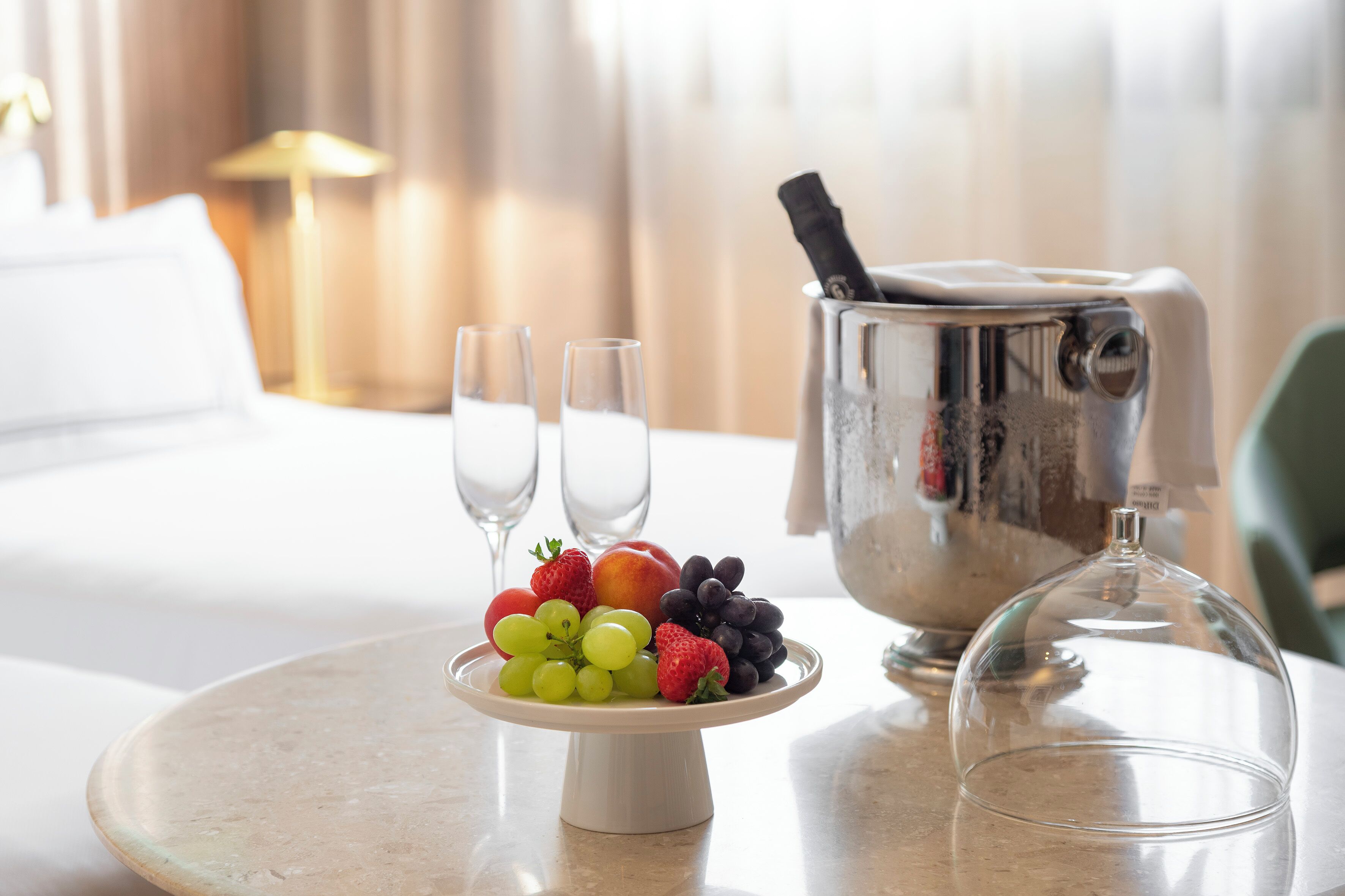 Una escena de desayuno con una bandeja de frutas, dos vasos y un cubo para champán sobre una mesa.