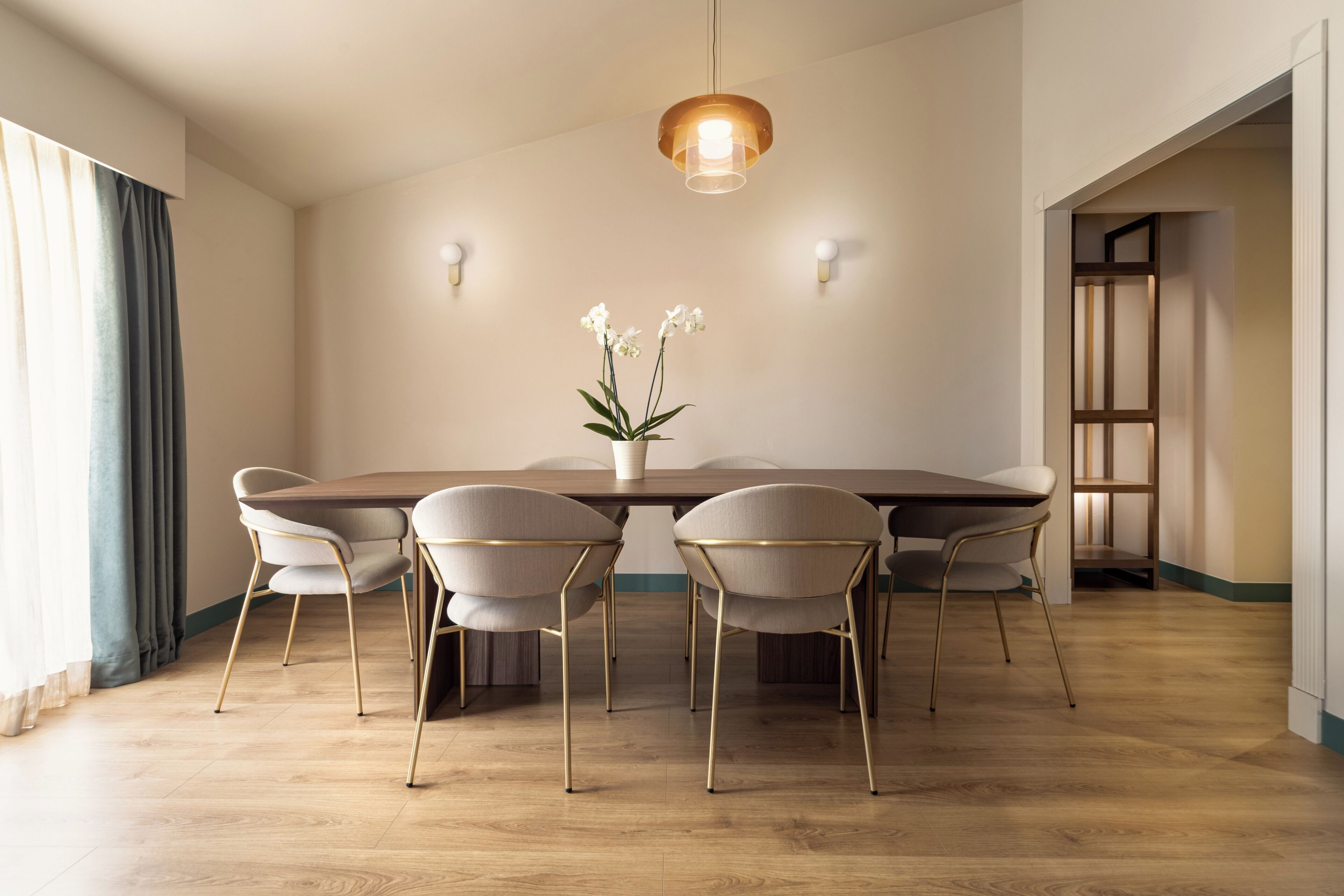 A dining area with a wooden table, six chairs, a vase with flowers, and a hanging light fixture.