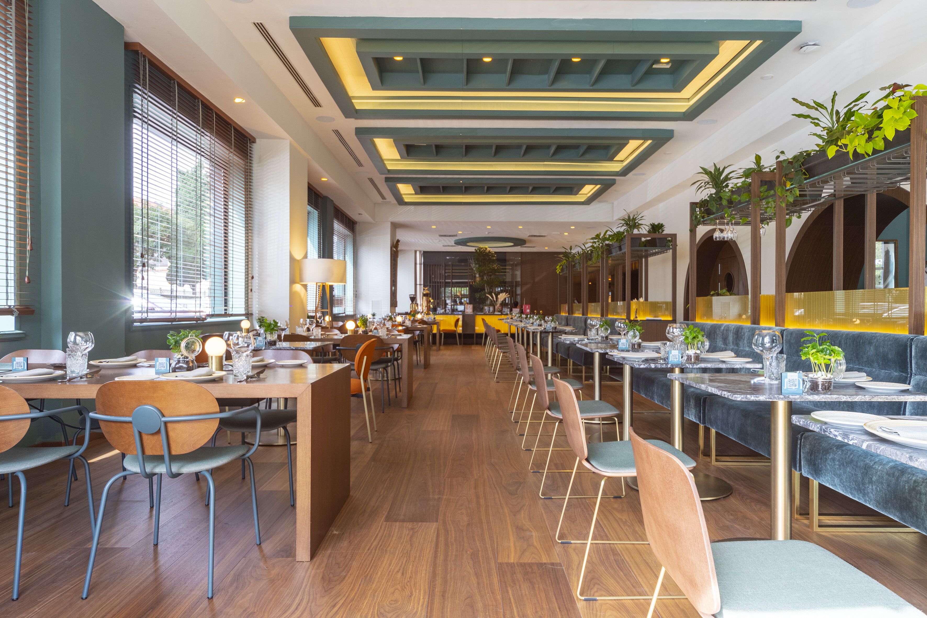 A spacious restaurant with long tables and booths, wooden flooring, and modern ceiling design.