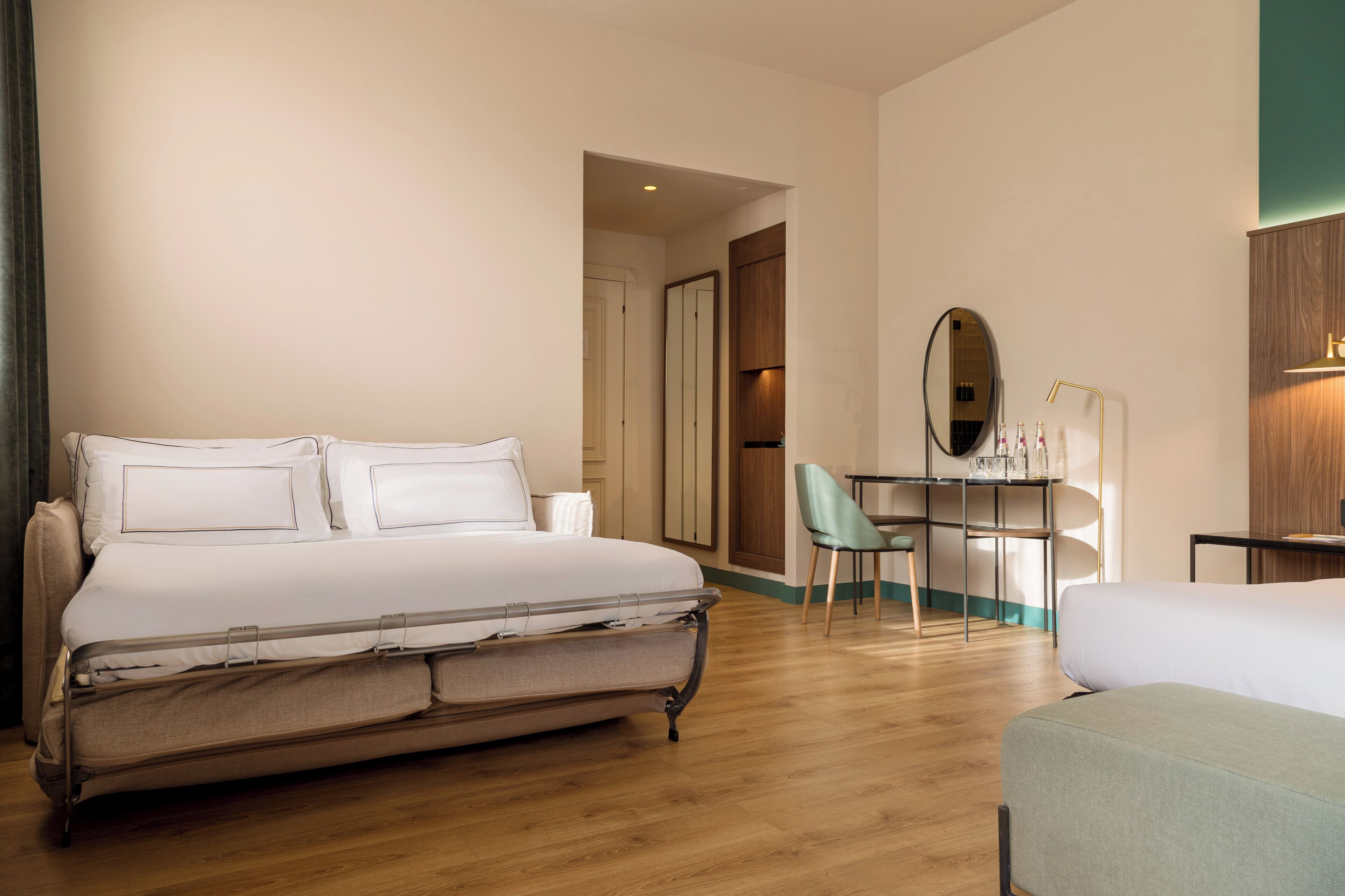 A hotel room with a bed, a desk, a chair, and a mirror.