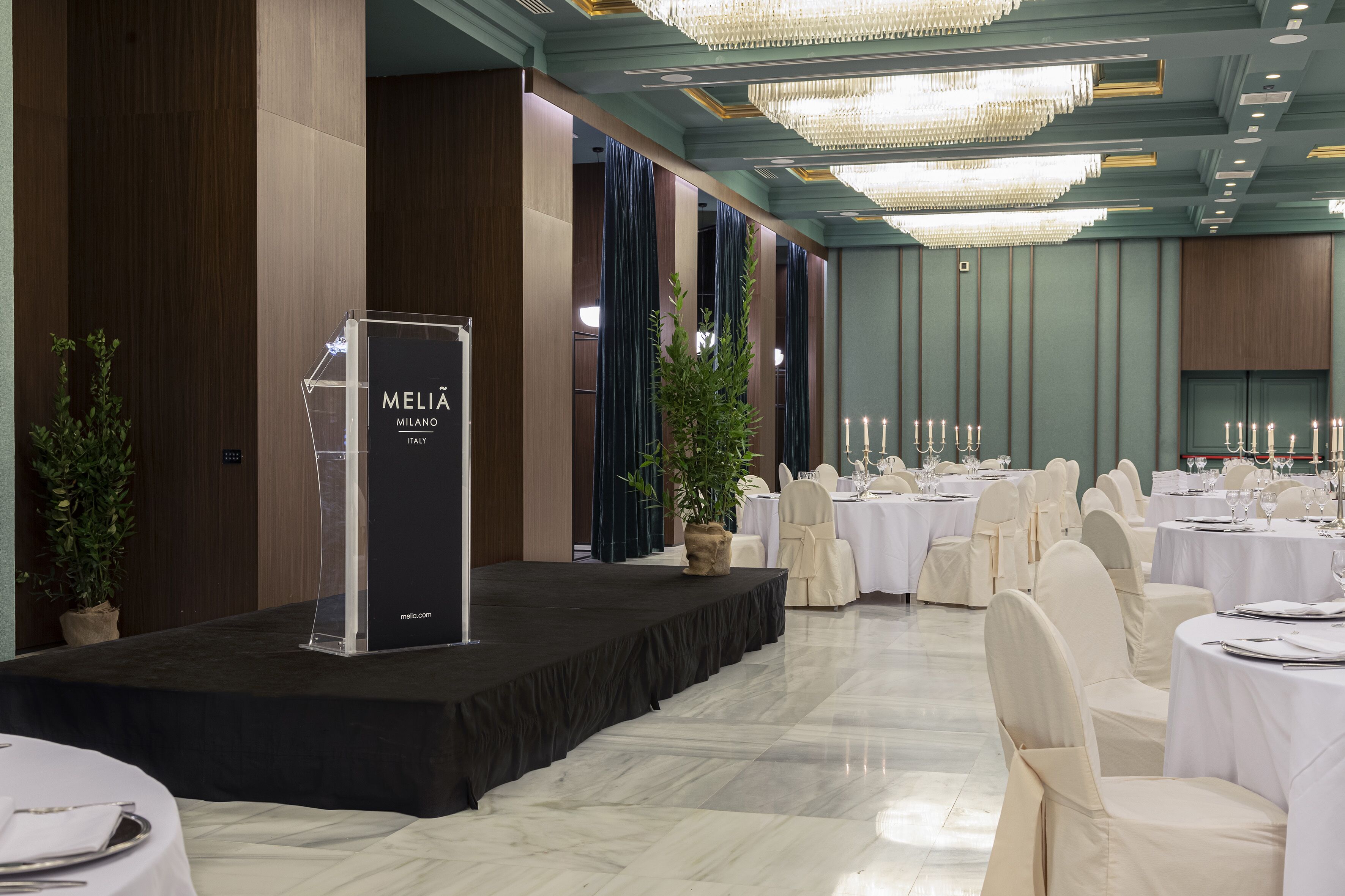 Une salle de banquet dotée d’une scène, de chaises blanches et de tables préparées pour un événement officiel.