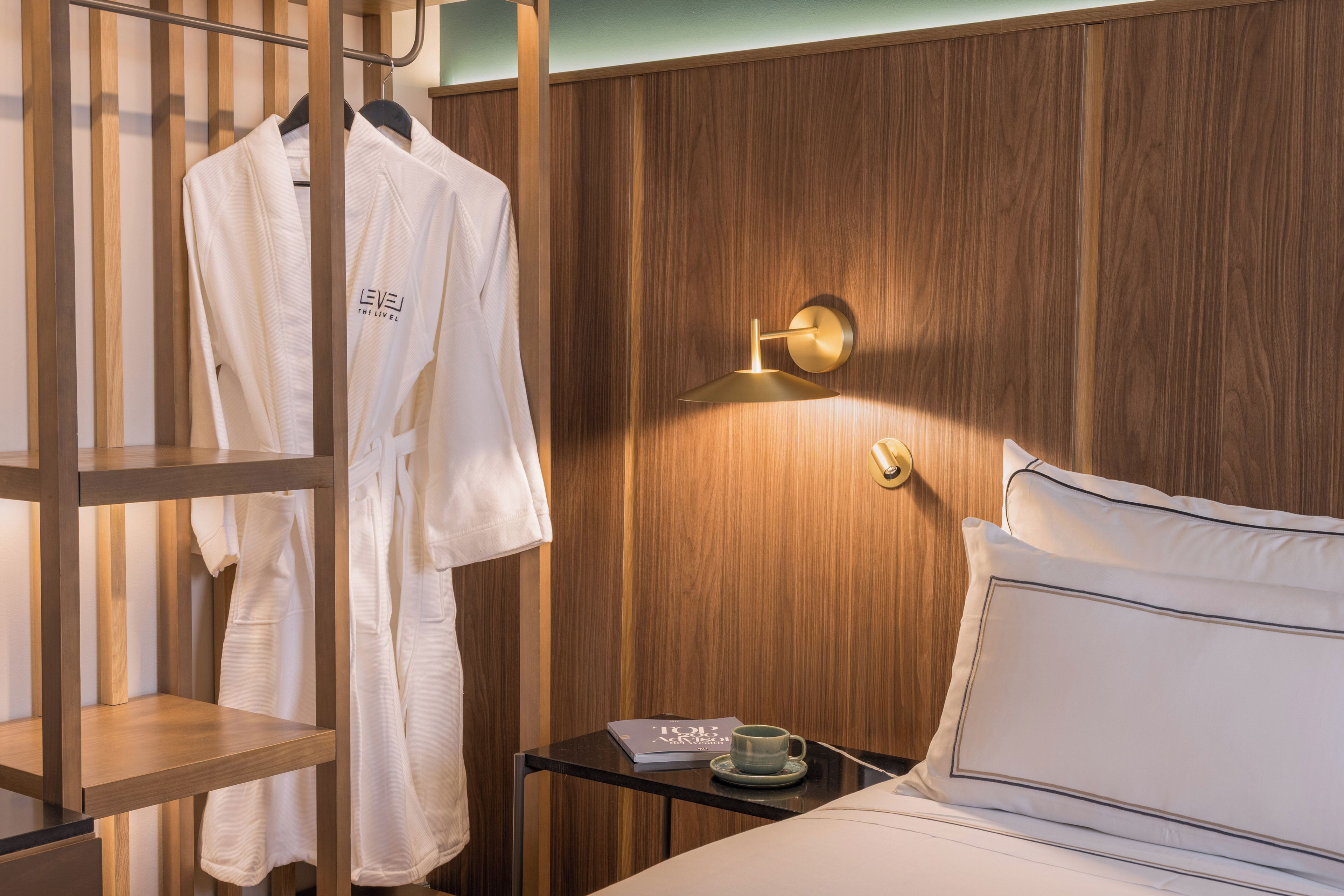 A hotel room with a wooden panel wall, a bedside table with a cup and a menu, and a hanging robe with a logo.