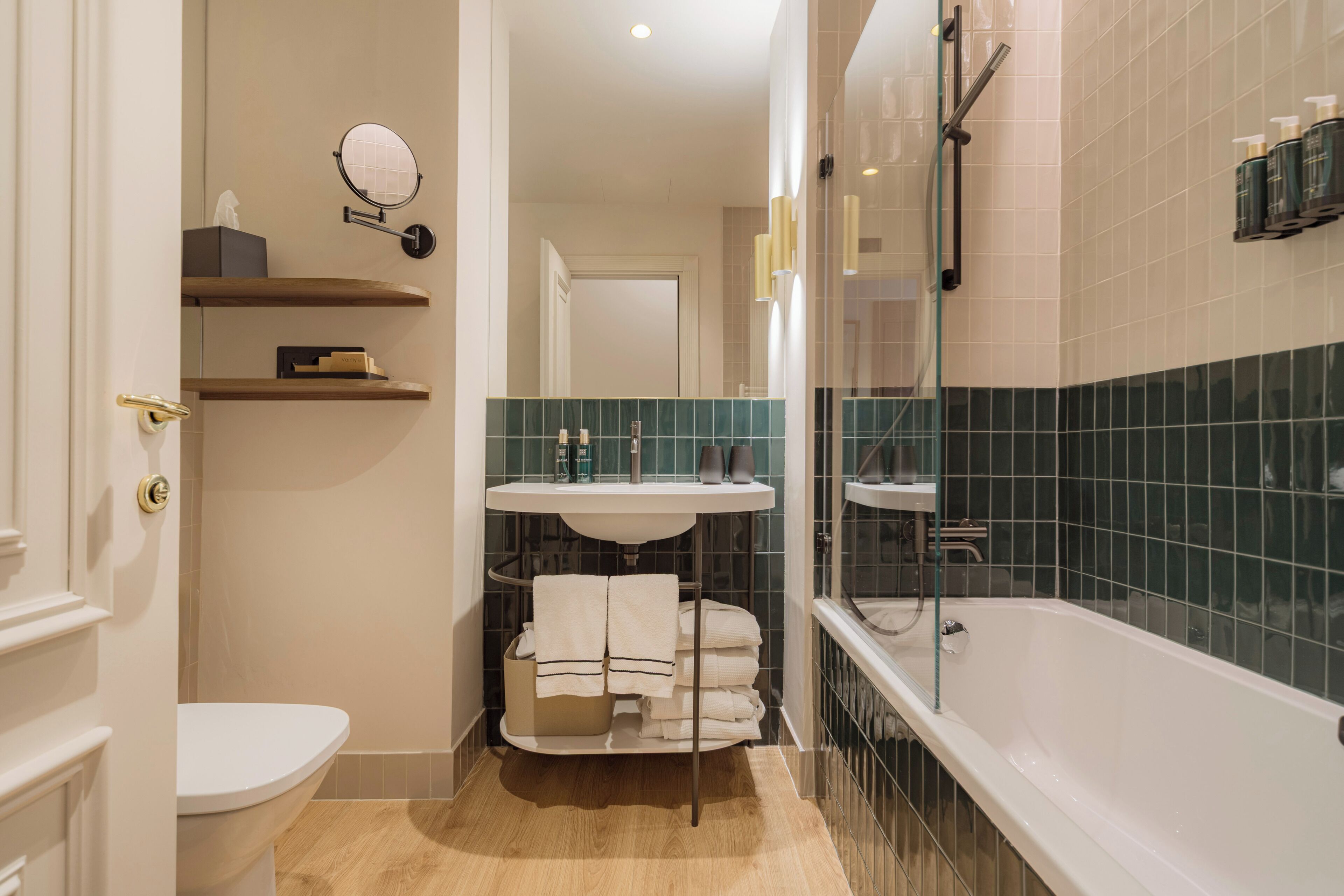 Een moderne badkamer met toilet, wastafel en bad. Er zijn planken met toiletartikelen en een handdoekhouder.