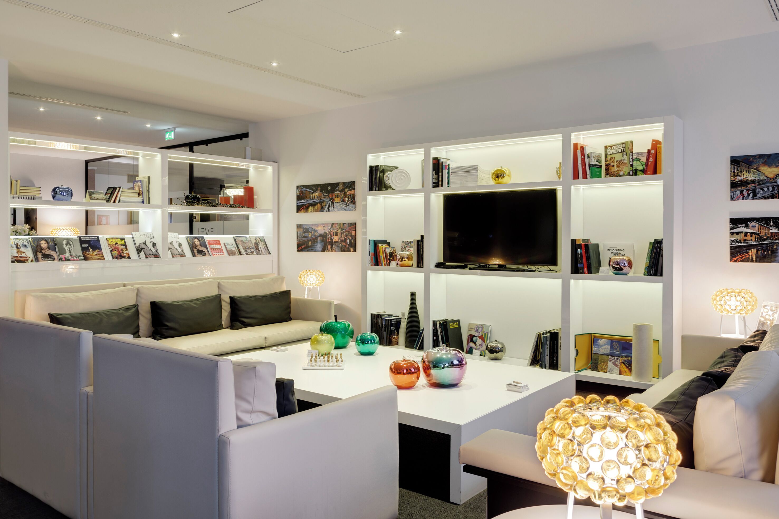 Una sala de estar moderna con un sofá, una mesa de centro con objetos decorativos, una estantería y un televisor de pantalla plana.