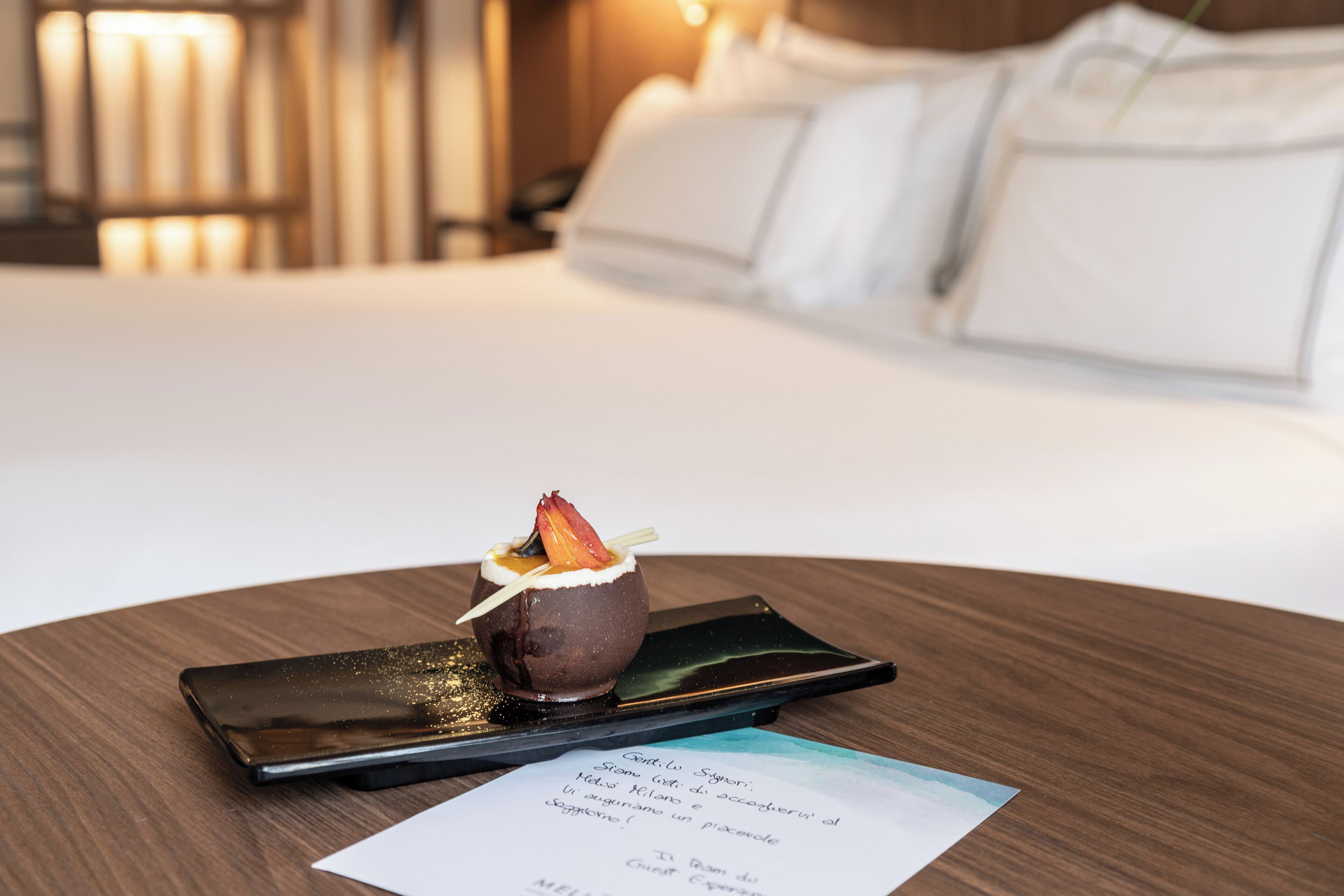 Un dessert su un vassoio con un menu appoggiato su un tavolo di legno in una camera d'albergo.