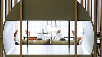 A modern, minimalist room with a curved seating area, a glass table, and a view of a dining area through a wooden partition.