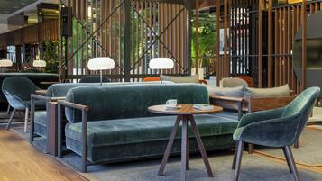 A modern lounge area with a green sofa, two armchairs, a small round table, and a coffee cup.