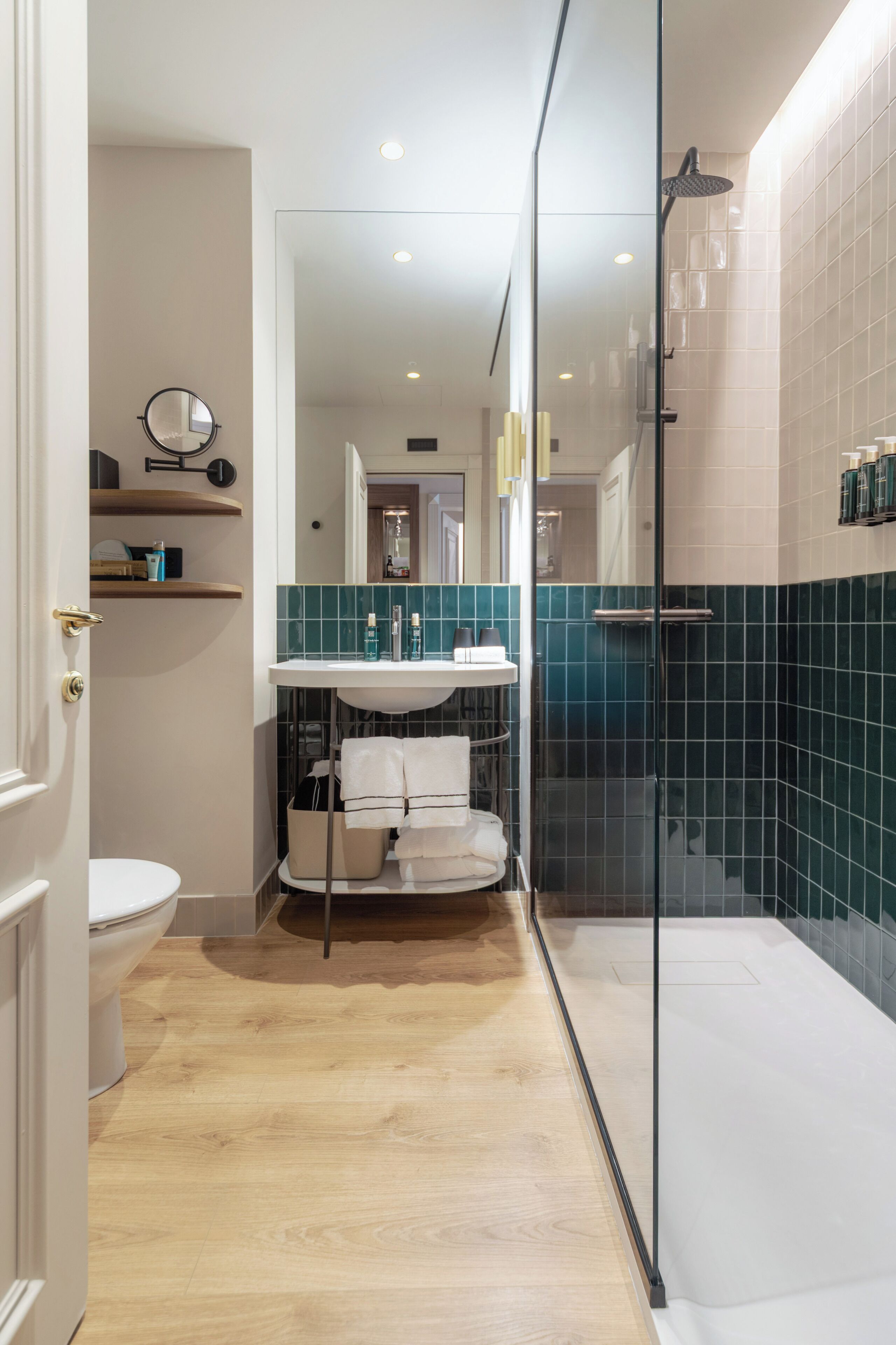 Un baño moderno con cabina de ducha de vidrio, un lavamanos blanco y suelo de madera.