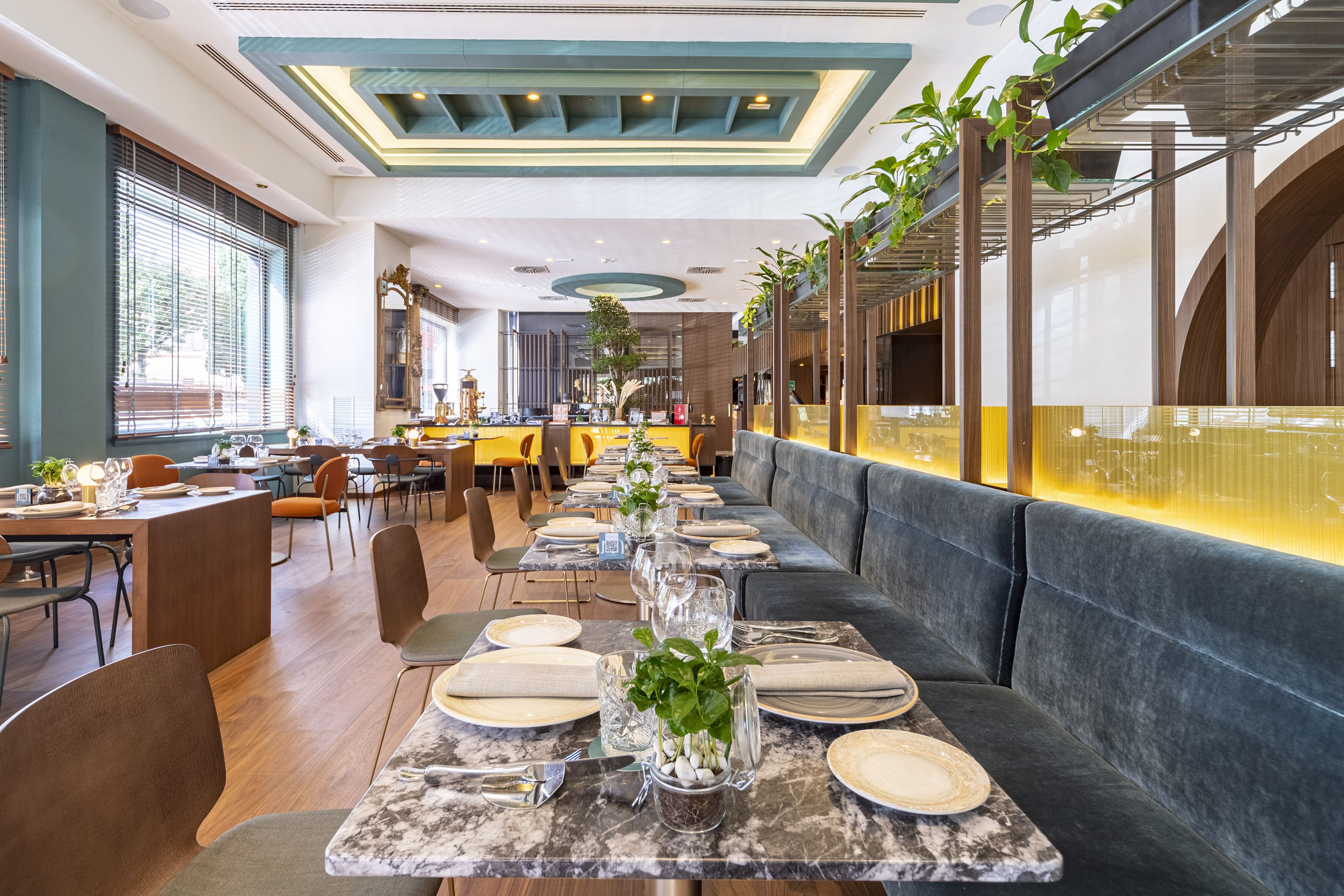 A restaurant with a long dining table set for a meal, a bar area, and a seating section with cushioned benches.