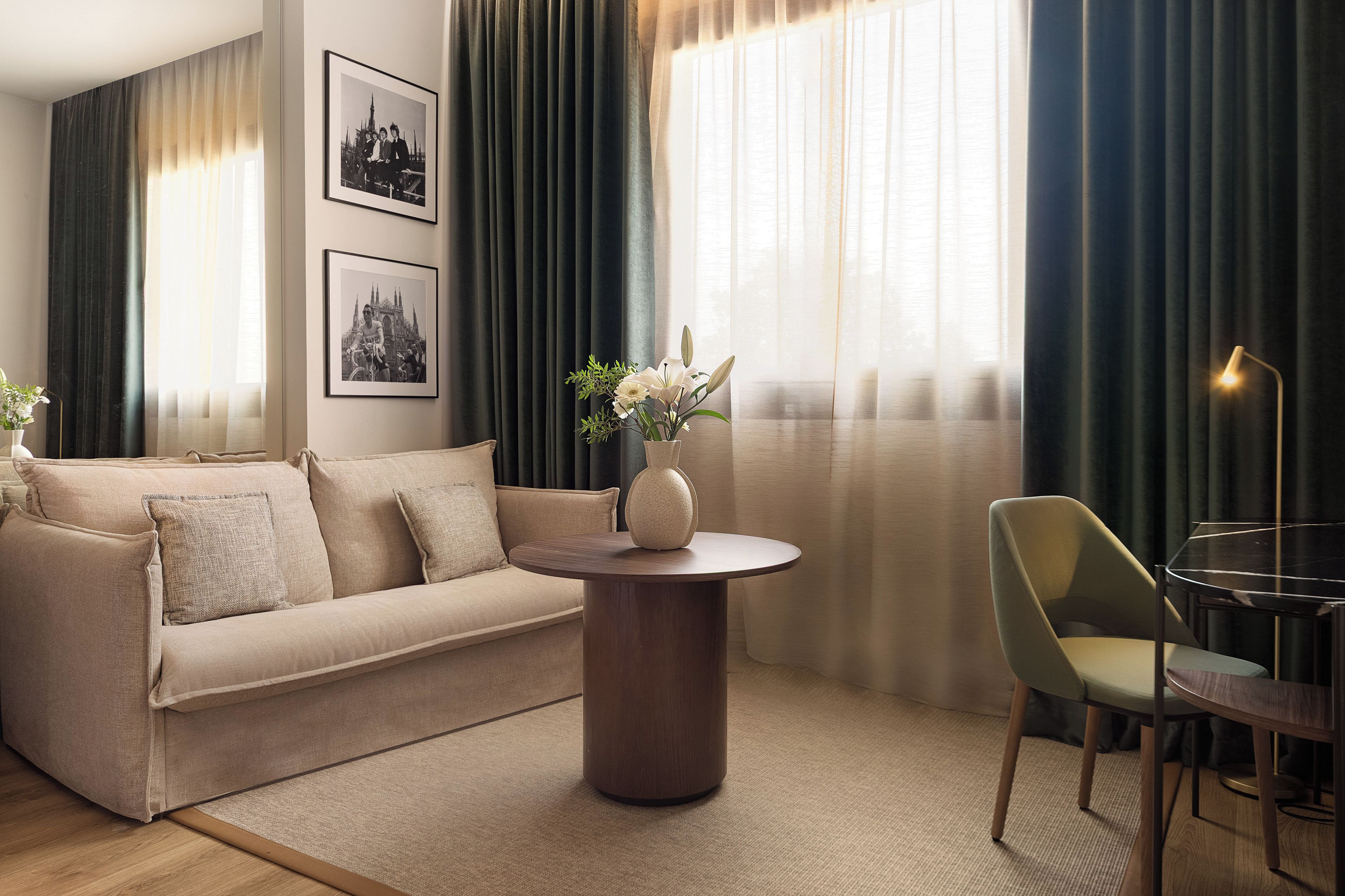 Un salon moderne avec un canapé beige, une table basse ronde en bois, un vase avec des fleurs, un fauteuil vert et une lampe.