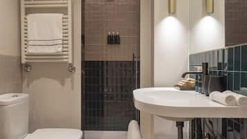 Un baño moderno con inodoro, bidé y lavamanos. Incluye un perchero, un espejo y un cesto de almacenamiento.