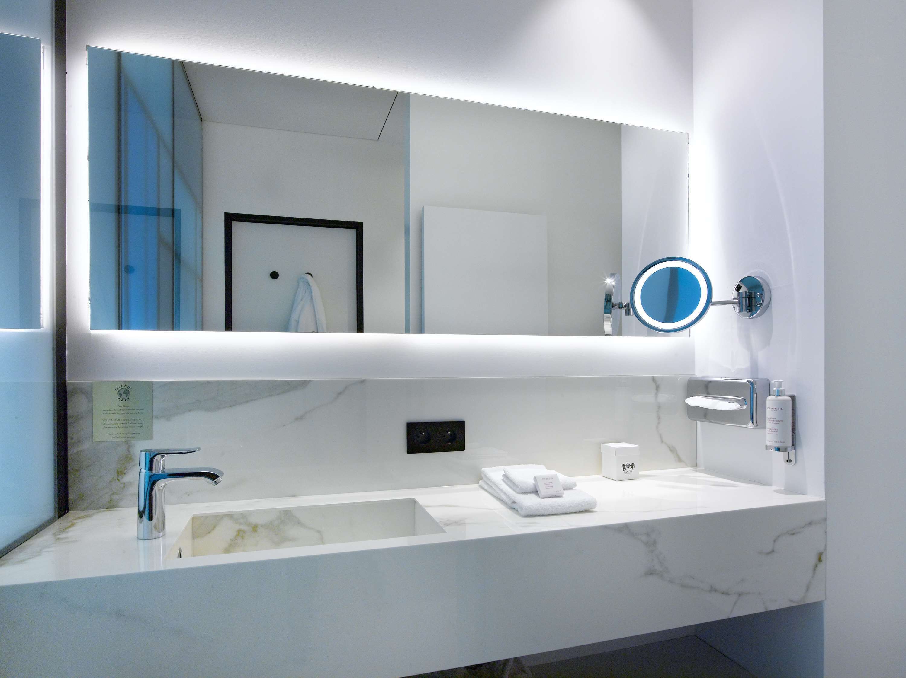 A modern bathroom with a large mirror, a sink, and a towel rack.