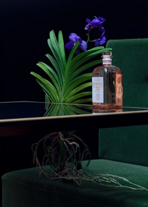 A bottle of Copper Head whiskey on a reflective surface with a green chair and a plant in the background. - Hotel Damier (Kortrijk)