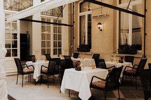 A restaurant with multiple tables and chairs, large windows, and a decorative wall light.