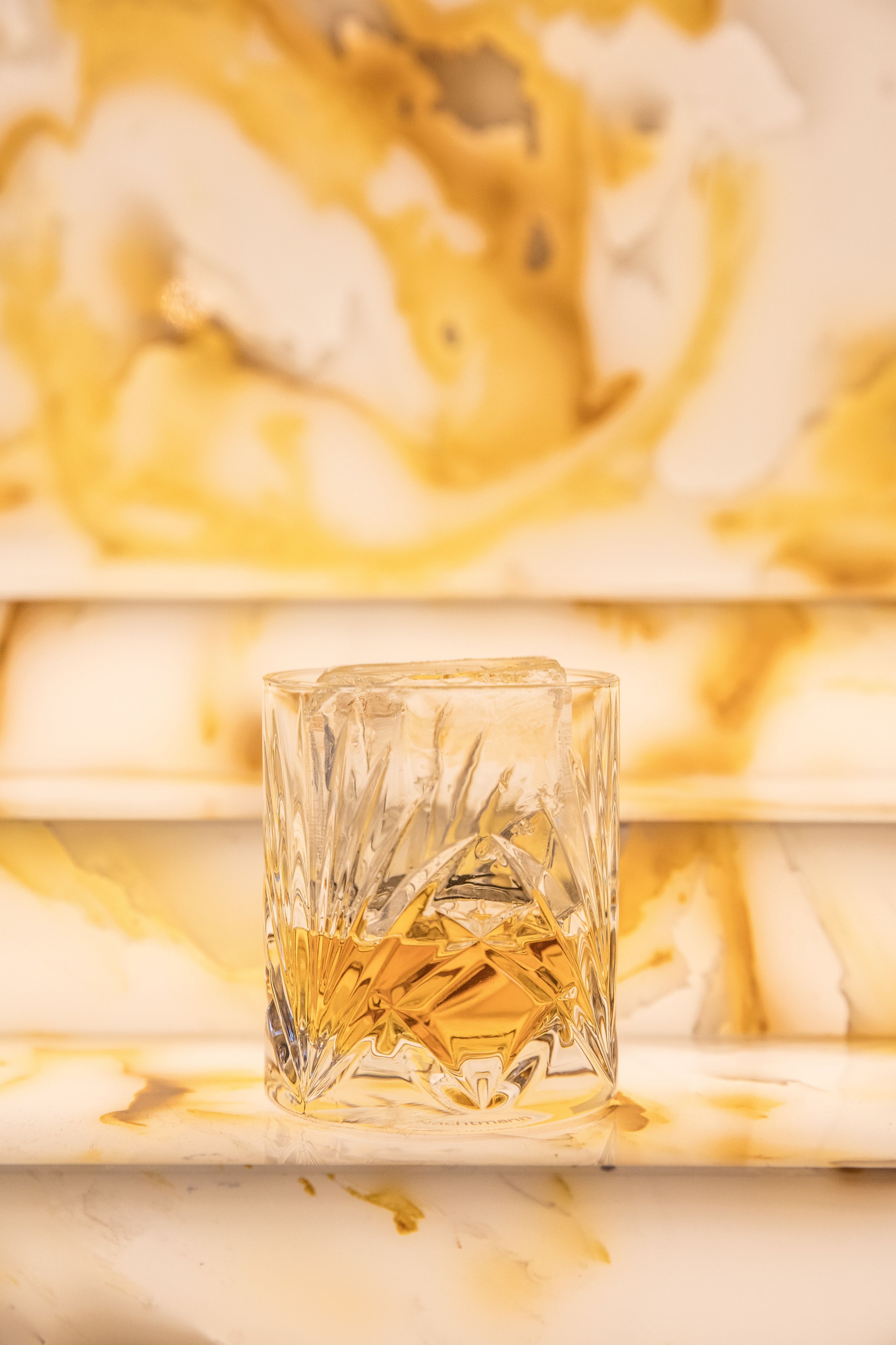 A clear glass with a geometric pattern, placed on a white surface with a golden design in the background.