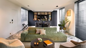 A modern living room with a green sofa, a round coffee table, and a dining area with a dark cabinet. - Hotel Damier (Kortrijk)