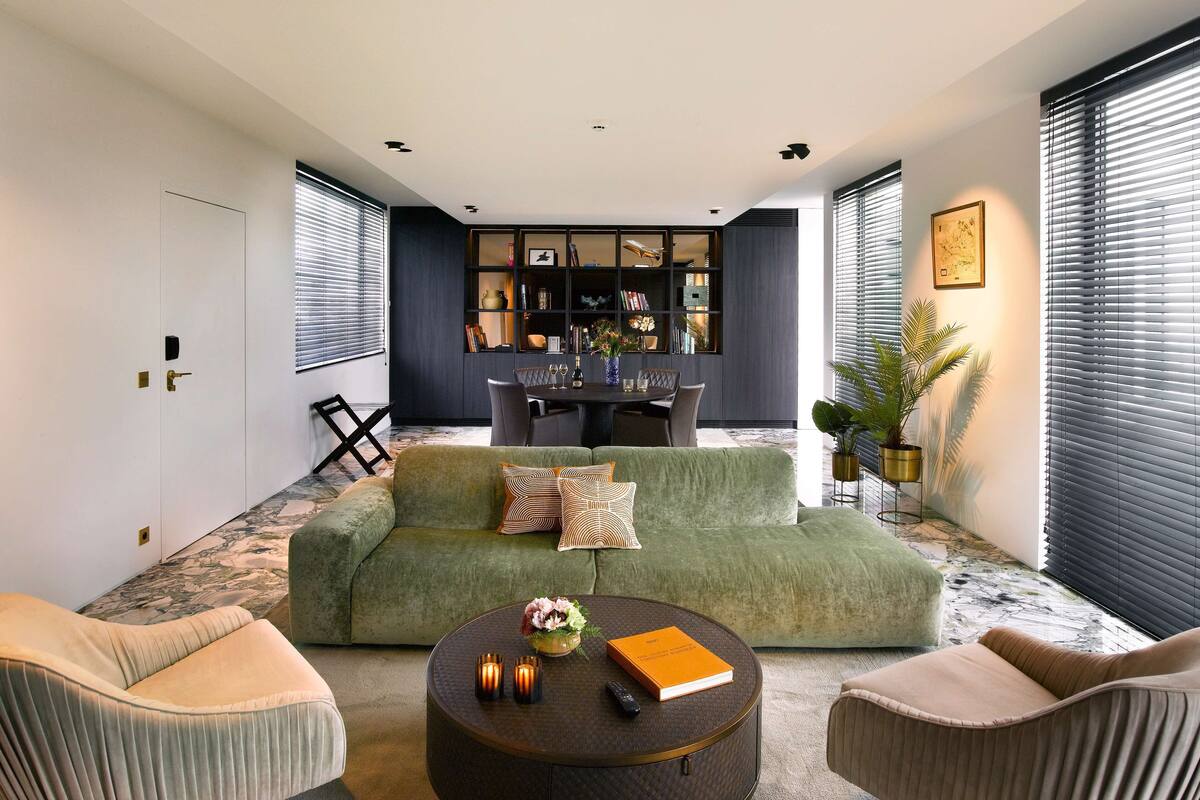 Een moderne woonkamer met een groene bank, een ronde salontafel en een eethoek met een donkere kast.