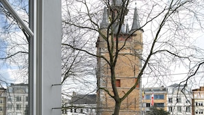 A view from a window overlooking a brick tower, a tree, and buildings in the background. - Hotel Damier (Kortrijk)